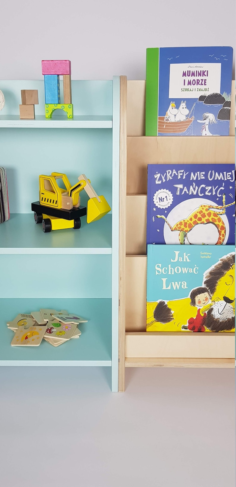 May include: A light blue bookshelf with three shelves, a wooden book holder with three slots, and various children's books. The bookshelf is filled with toys, including a yellow toy excavator, a set of wooden blocks, and a puzzle.