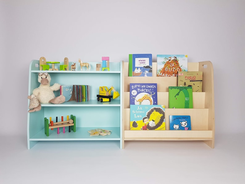 Puede incluir: Dos estanter&iacute;as de libros de madera, una azul claro y otra de madera natural, llenas de libros para ni&ntilde;os. La estanter&iacute;a azul tiene un pato de peluche y otros juguetes en los estantes. Las estanter&iacute;as son una excelente manera de organizar y exhibir libros para ni&ntilde;os.