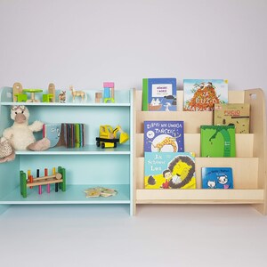 May include: Two wooden bookshelves, one light blue and one natural wood, filled with children's books. The blue bookshelf has a stuffed duck and other toys on the shelves. The bookshelves are a great way to organize and display children's books.