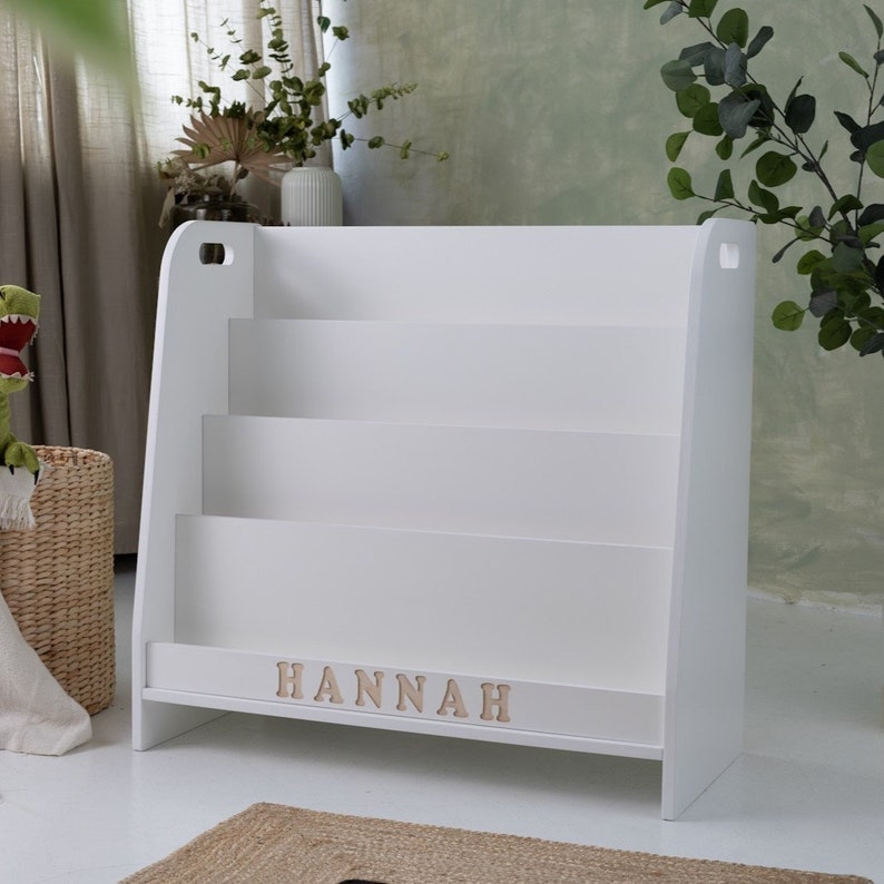 Pu&ograve; includere: Libreria in legno bianco con tre ripiani e una targhetta con il nome "HANNAH".