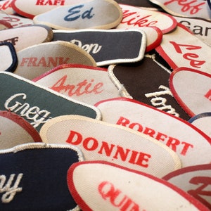 May include: A close-up of a pile of fabric patches with various names embroidered on them in white thread. The patches are in various colors, including red, white, blue, green, and black. The names on the patches include "Don", "Tony", "Clint", "Robert", "Donnie", "Greg", "Antie", "Rick", "Gary", "Jeff", "Ed", "Frank", "Rafi", "Carl", "Les", and "Mike".