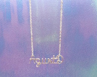 May include: A silver chain necklace with a wire-wrapped pendant that says "August" in cursive.