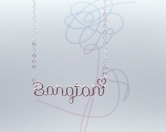 May include: Silver necklace with a wire-shaped pendant that says "Bangtan" with a small heart at the end.