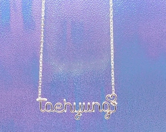 May include: Silver chain necklace with the name "Taehyung" spelled out in wire with a heart at the end.