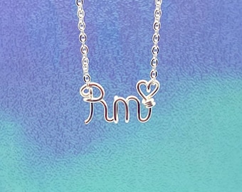 May include: A silver necklace with the name "Rm" spelled out in wire, with a small heart charm between the letters.