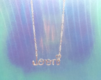 May include: A silver chain necklace with the word "loon" spelled out in wire, with a small heart charm at the end.