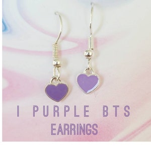 May include: A pair of silver dangle earrings with purple heart charms. The earrings are labeled "I Purple BTS Earrings".