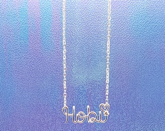 May include: Silver necklace with the word "Hobi" written in cursive with a small heart charm.