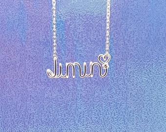 May include: Silver necklace with the name "Jimin" spelled out in wire with a small heart charm.