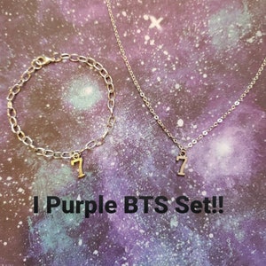 May include: A silver chain necklace and bracelet set with a silver charm of the number 7. The text "I Purple BTS Set!" is written below the jewellery.