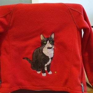 May include: Red fleece jacket with an embroidered black and white cat on the back.