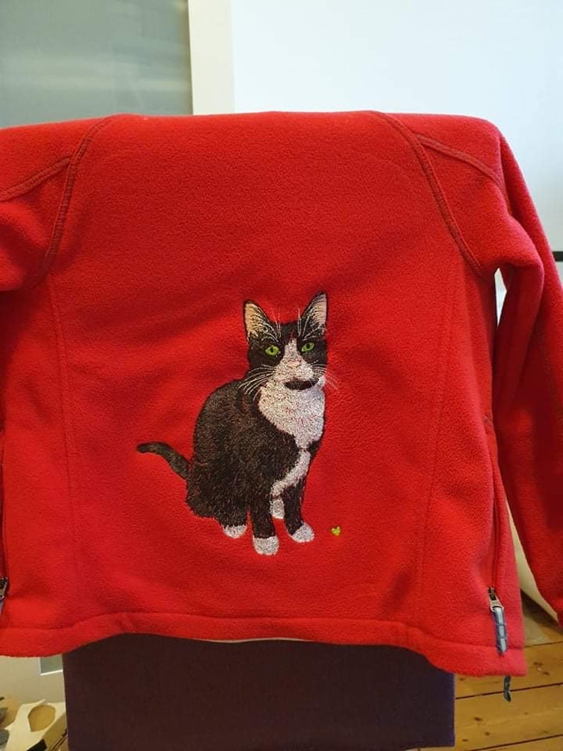 May include: Red fleece jacket with an embroidered black and white cat on the back.