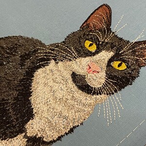 May include: Embroidered black and white cat with yellow eyes on a light blue background.
