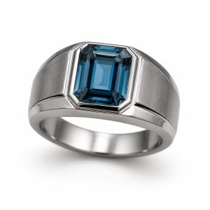 Op de afbeelding: Een zilveren ring met een grote, rechthoekige, blauwe edelsteen. De edelsteen is gezet in een bezel setting en de band heeft een geborstelde afwerking. De ring is een klassiek ontwerp.