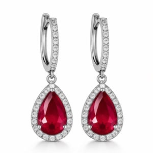 Op de afbeelding: Zilveren oorringen met een druppelvormige rode edelsteen hanger. De hanger is omgeven door een halo van kleine, heldere edelstenen. De oorbellen worden gepresenteerd tegen een witte achtergrond.