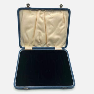 Może przedstawiać: Otwarty, prostokątny pojemnik na biżuterię z niebieskim zewnętrzem i czarnym aksamitnym wnętrzem. Pudełko jest wyłożone kremową tkaniną i ma zawiasy w kolorze mosiądzu. Pudełko jest przeznaczone do przechowywania biżuterii.