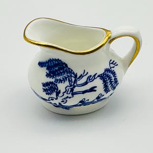 Puede incluir: Un pequeño creamer blanco con un patrón de sauce azul y blanco y un borde dorado.