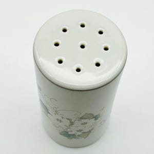 May include: White ceramic salt shaker with a floral design and nine holes on the top.