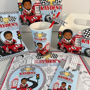 May include: A collection of racing-themed party supplies. Includes a cup, placemat, favor bags, and decorations featuring a child in a red race car. The text "Kayden's First Lap" is visible on several items, along with checkered flags and a gas pump.