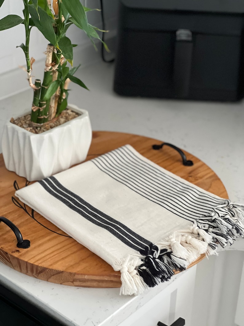 Puede incluir: Una toalla de algod&oacute;n a rayas blancas y negras con flecos en una bandeja de madera. La toalla est&aacute; doblada y tiene un patr&oacute;n de rayas blancas y negras.