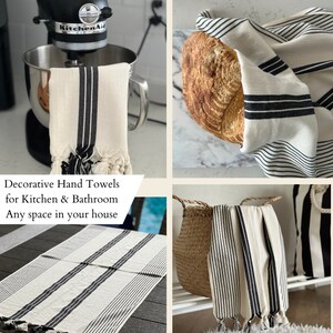 Puede incluir: Conjunto de cuatro toallas de mano blancas con rayas negras y borlas. Las toallas se muestran en varios entornos, incluyendo en una encimera de cocina, en una cesta y drapeadas sobre una hogaza de pan. Las toallas son decorativas y se pueden usar en la cocina o en el ba&ntilde;o.