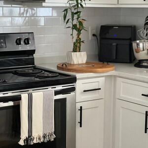 Puede incluir: Un horno de acero inoxidable con una toalla de cocina a rayas blancas y negras colgada del asa. El horno est&aacute; en una cocina moderna con gabinetes blancos y herrajes negros.