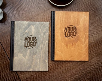 May include: Two wooden menu covers with black edging. The covers are made of light wood and dark wood. Both covers have the text "YOUR LOGO" engraved on them.
