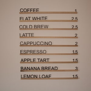 K&ouml;nnte beinhalten: Eine Speisekarte mit Preisen f&uuml;r Kaffee, Espresso-Getr&auml;nke und Backwaren. Die Preise sind in Euro angegeben. KAFFEE 1&euro;, FLATTER WEISS 2,50&euro;, KALTER BRUH 2,50&euro;, LATTE 2&euro;, CAPPUCCINO 2&euro;, ESPRESSO 1,50&euro;, APFELTARTE 1,50&euro;, BANANENBROT 3&euro;, ZITRONENKUCHEN 1,50&euro;