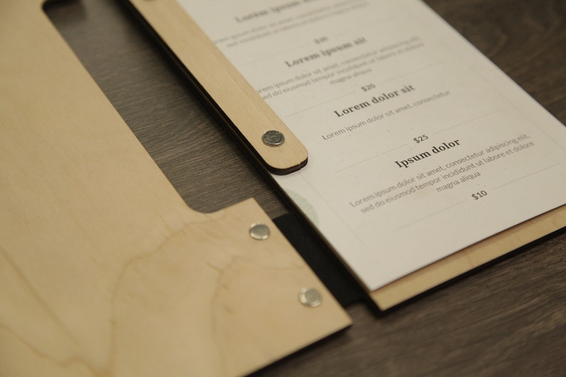 May include: A wooden menu holder with a black strap and metal fasteners. The menu is printed on white paper with the text "Lorem ipsum", "Lorem dolor sit", "Ipsum dolor", and prices in dollars.
