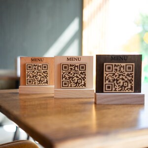 Peut inclure: Trois pancartes de table en bois avec le mot "MENU" et un code QR noir et blanc imprimé dessus. Les pancartes sont sur une table en bois.