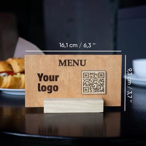 May include: A wooden menu sign with a QR code, the text "MENU" and "Your logo" printed on it. The sign is 6.3 inches wide and 3.7 inches tall.