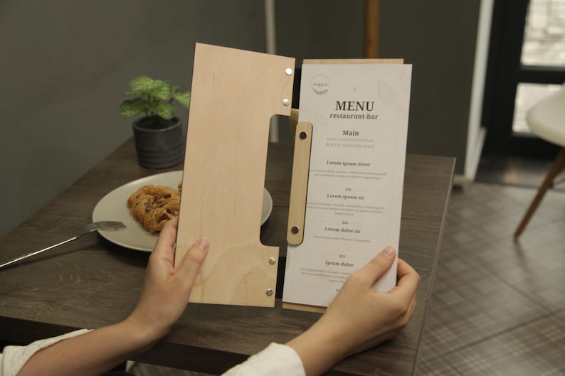 May include: A wooden menu holder with a white paper menu insert. The menu has the text "MENU restaurant-bar" and lists "Main" with several menu items.