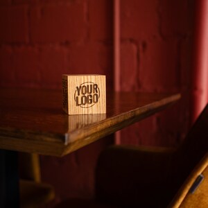 May include: A wooden block with the text "YOUR LOGO" engraved on it. The block is sitting on a wooden table in front of a red brick wall.
