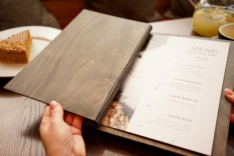 May include: A wooden menu cover with a white paper menu inside. The menu has the text "MENU restaurant bar Share" and lists different food items with prices.