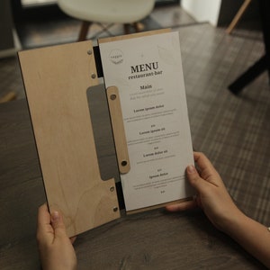 May include: A wooden menu holder with a white paper menu insert. The menu is titled "MENU restaurant-bar" and lists "Main" with several food items and prices.