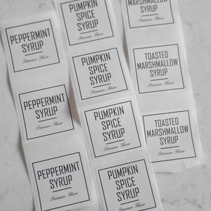 May include: Nine white labels with black text for different syrup flavors. The labels read "Peppermint Syrup", "Pumpkin Spice Syrup", and "Toasted Marshmallow Syrup".