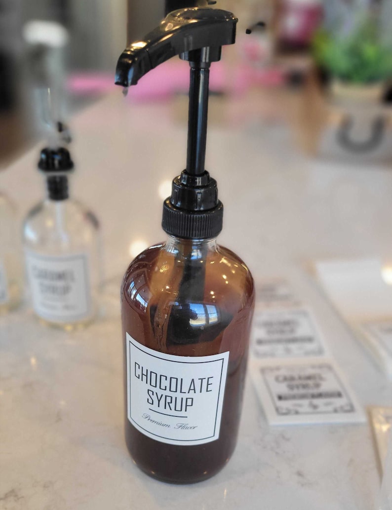 May include: A glass bottle with a black pump dispenser filled with dark brown chocolate syrup. The label reads "Chocolate Syrup" and "Premium Flavor".