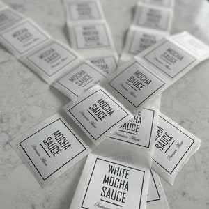May include: A stack of white labels with black text that reads "Mocha Sauce" and "White Mocha Sauce" with the words "Premium Flavor" printed below.