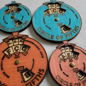 Puede incluir: Cuatro herramientas de teor&iacute;a musical de madera en forma de c&iacute;rculo de quintas. Dos est&aacute;n pintadas de azul claro y dos de naranja claro. Cada c&iacute;rculo tiene un dial giratorio con notas y acordes musicales.