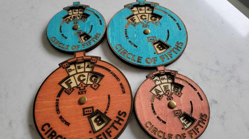 Puede incluir: Cuatro herramientas de teor&iacute;a musical de madera en forma de c&iacute;rculo de quintas. Dos est&aacute;n pintadas de azul claro y dos de naranja claro. Cada c&iacute;rculo tiene un dial giratorio con notas y acordes musicales.