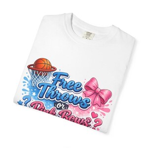 Puede incluir: Camiseta blanca con temática de baloncesto. El diseño incluye una pelota de baloncesto en una canasta, salpicaduras azules y rosas, un lazo rosa y el texto "Free Throws or Pink Bows?"