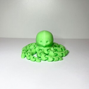 以下が含まれることがあります： 丸い頭と8本の関節のある触手を持つ、明るい緑色の3Dプリントされたタコです。