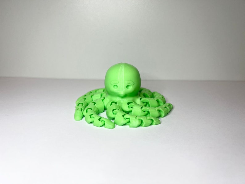 以下が含まれることがあります： 丸い頭と8本の関節のある触手を持つ、明るい緑色の3Dプリントされたタコです。