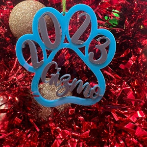 May include: Blue paw print Christmas ornament with the year 2023 and the name Gizmo written inside.