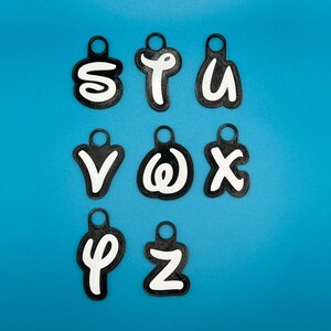 Op de afbeelding: Negen zwarte sleutelhangers met witte letters die het woord "STUVWXYZ" spellen op een blauwe achtergrond.