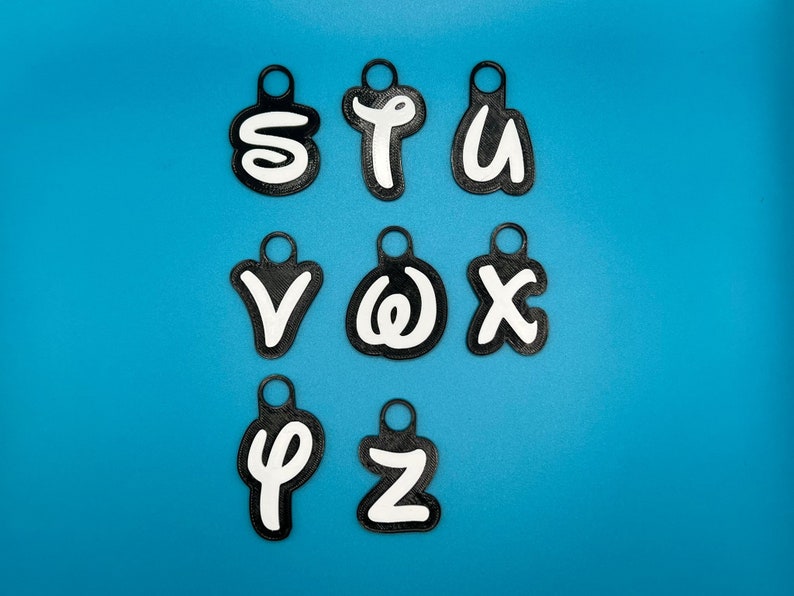 Op de afbeelding: Negen zwarte sleutelhangers met witte letters die het woord "STUVWXYZ" spellen op een blauwe achtergrond.