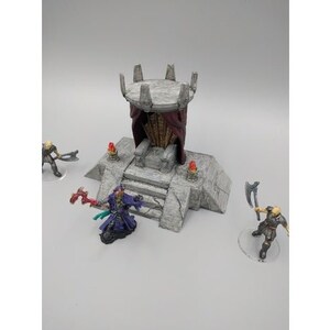 May include: A miniature stone throne with a red and black fabric canopy, set on a stone platform with steps. The throne is decorated with small, red torches.
