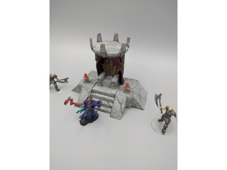 May include: A miniature stone throne with a red and black fabric canopy, set on a stone platform with steps. The throne is decorated with small, red torches.