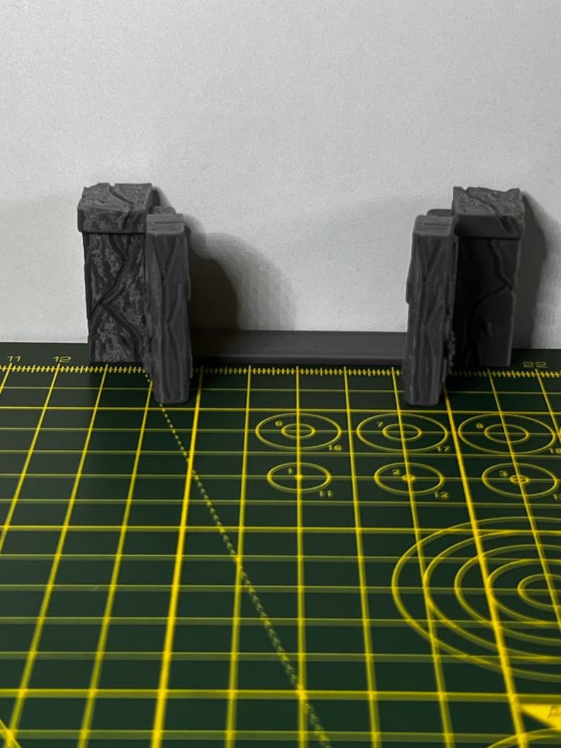 May include: Two gray, wooden, textured, miniature gate pieces on a green and yellow grid surface.
