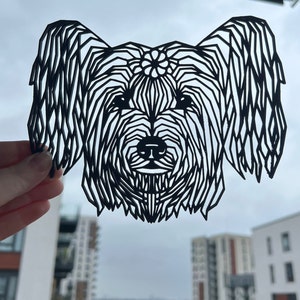 Op de afbeelding: Zwart-witte papieren uitsnijding van een hondenkop met ingewikkelde geometrische patronen.